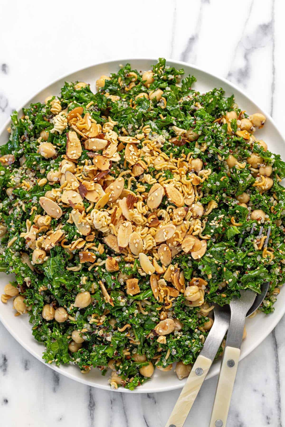 Large plate filled with sesame kale and quinoa salad topped with almonds, ramen, and sesame seeds.