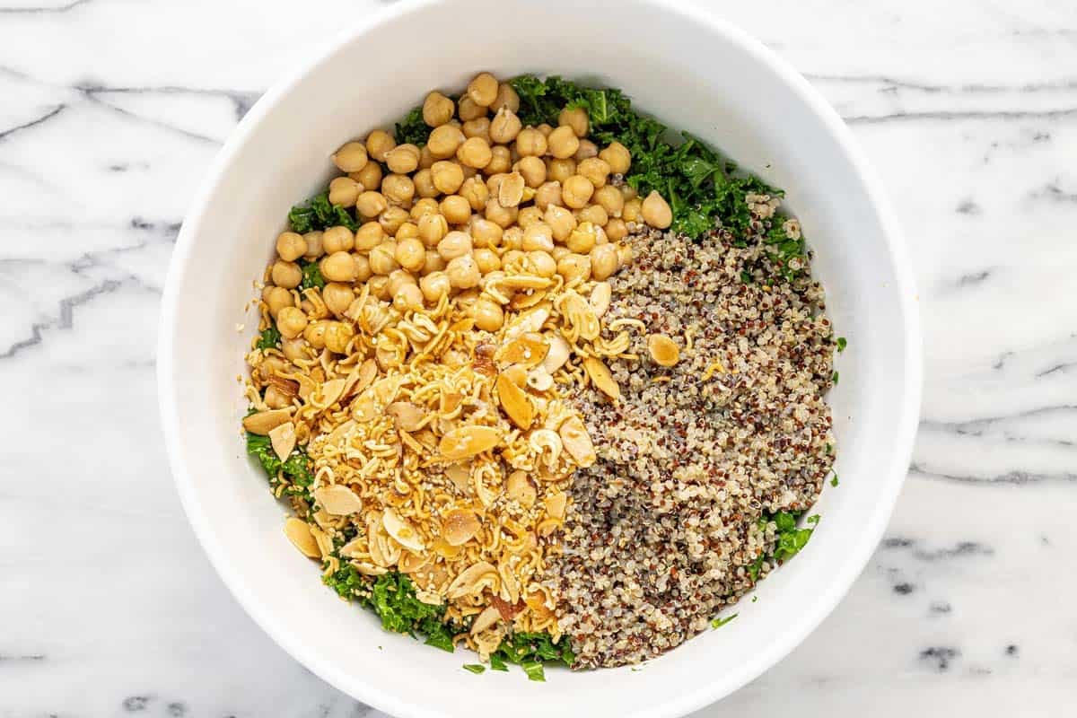 Bowl of massaged kale with chickpeas, quinoa, and crispy ramen, almonds, and sesame seeds.
