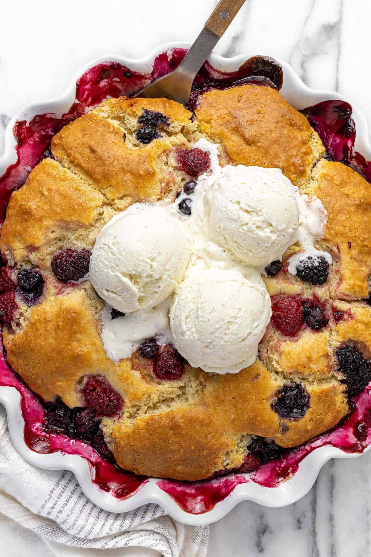 Large pie dish filled with homemade triple berry cobbler topped with three scoops of ice cream.