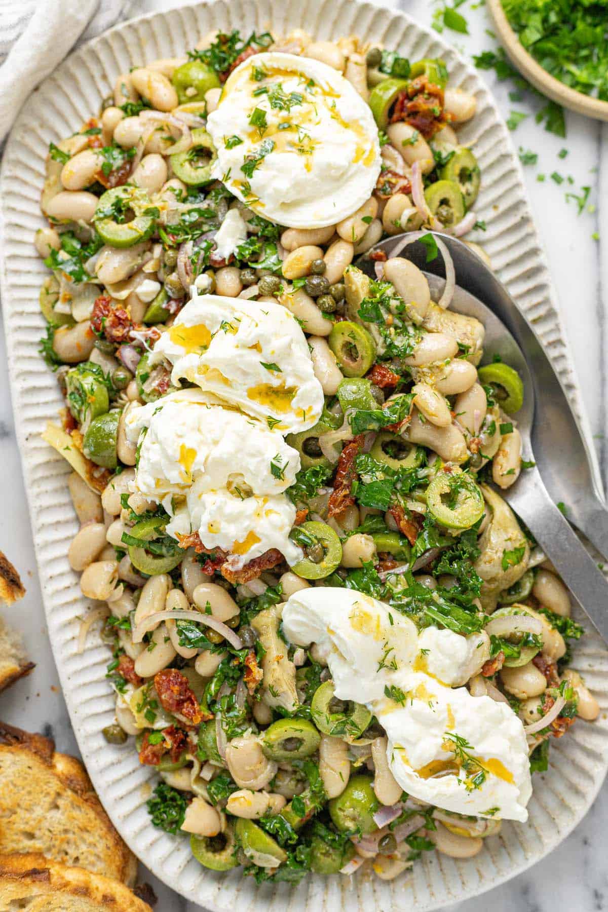 Large serving platter with marinated white bean salad garnished with burrata.