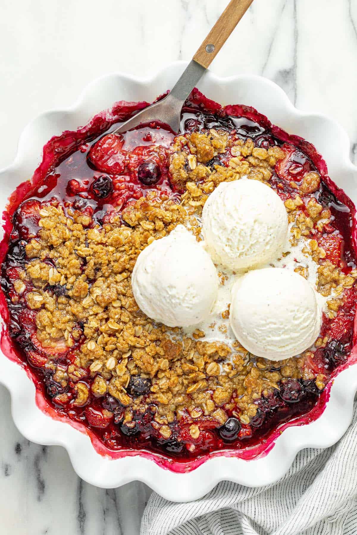 Large pie dish filled with homemade berry crisp topped with ice cream.