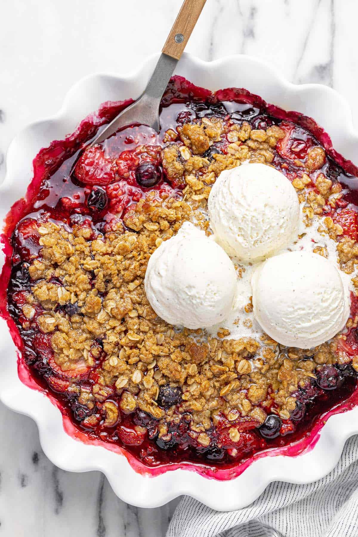 Large pie dish filled with homemade berry crisp topped with ice cream.