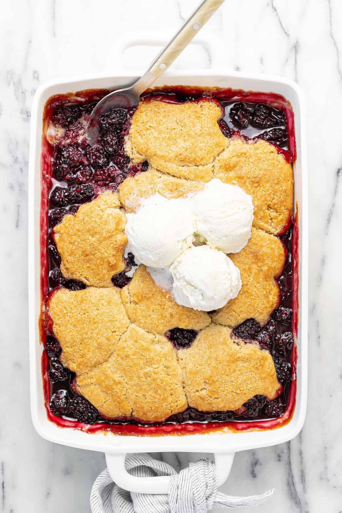 Large baking dish filled with blackberry cobbler topped with ice cream.