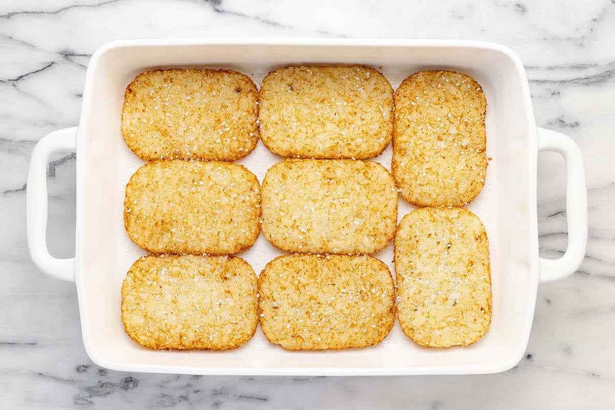 Large 9x13 baking dish filled with hash brown patties topped with salt.