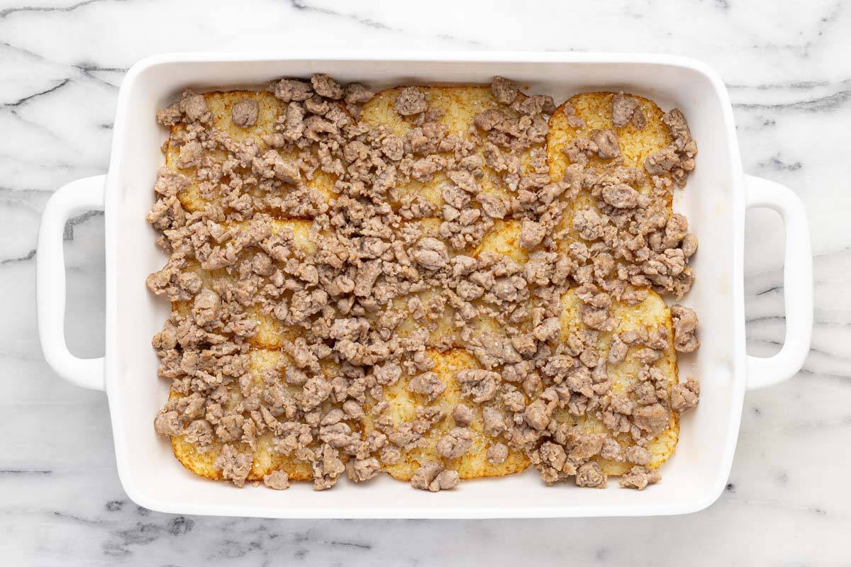 Cooked hash browns in a pan with cooked sausage.