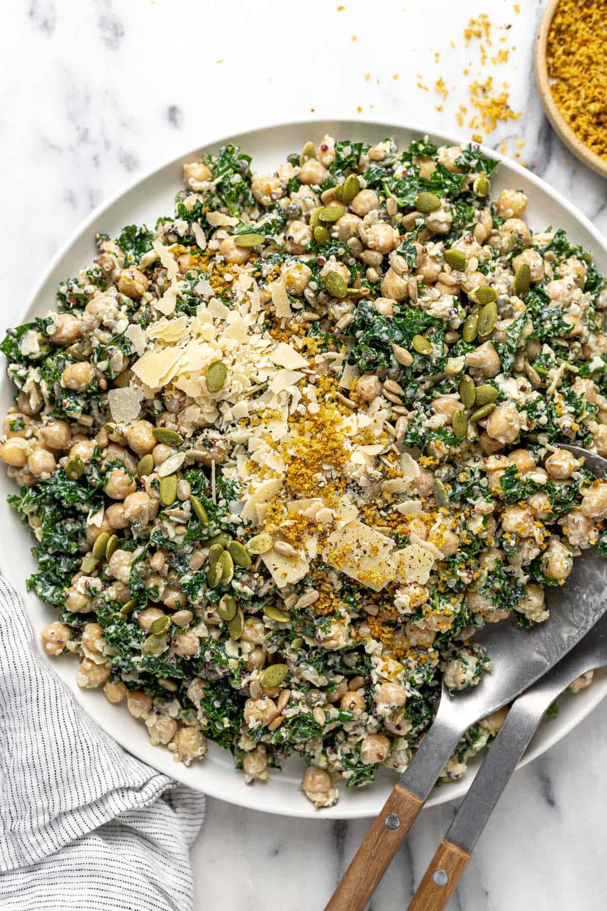 Large plate filled with dense bean Caesar salad garnished with Parmesan, breadcrumbs, and pumpkin seeds.