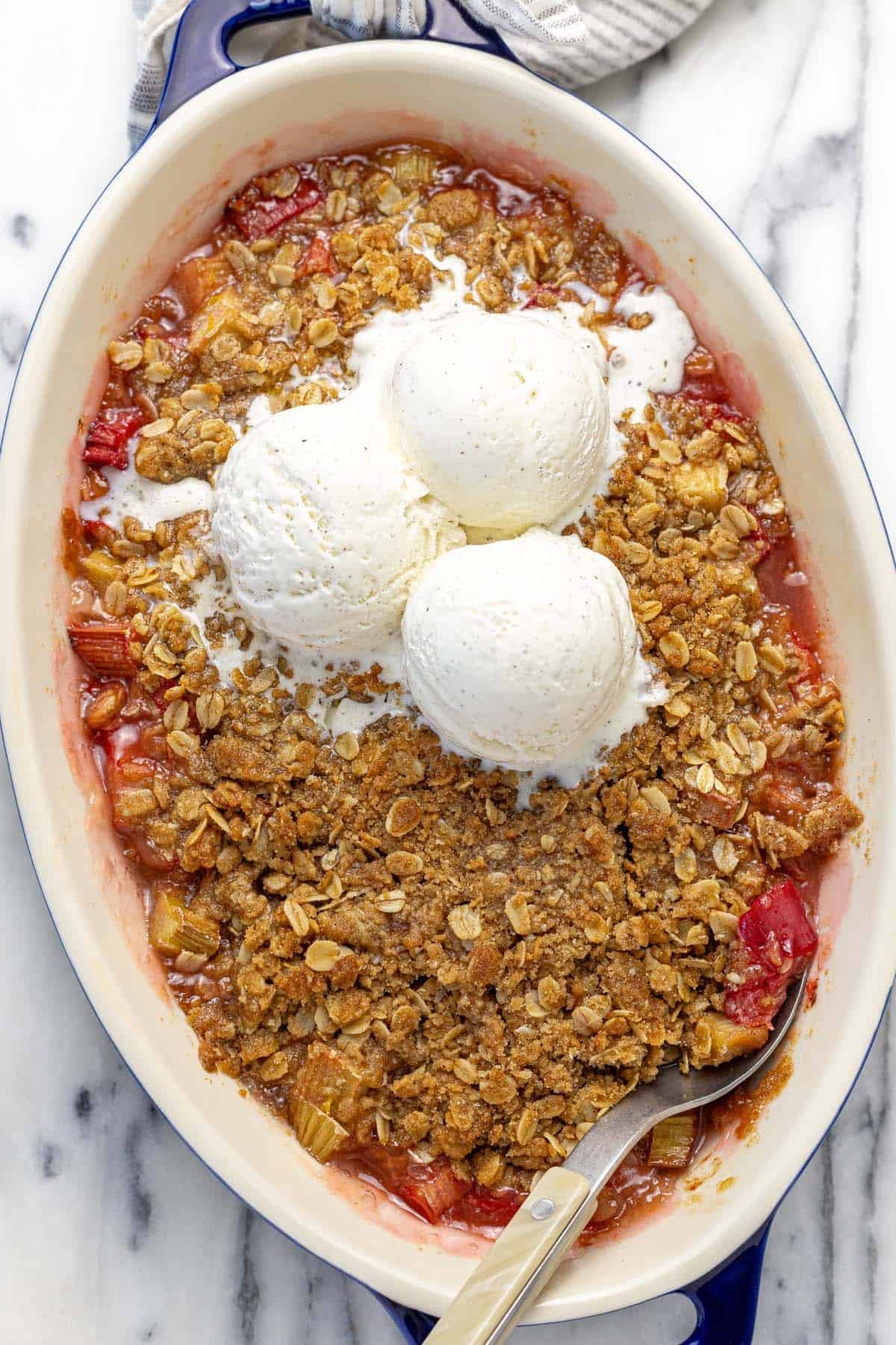 Baking dish with homemade rhubarb crisp topped with three scoops of ice cream.