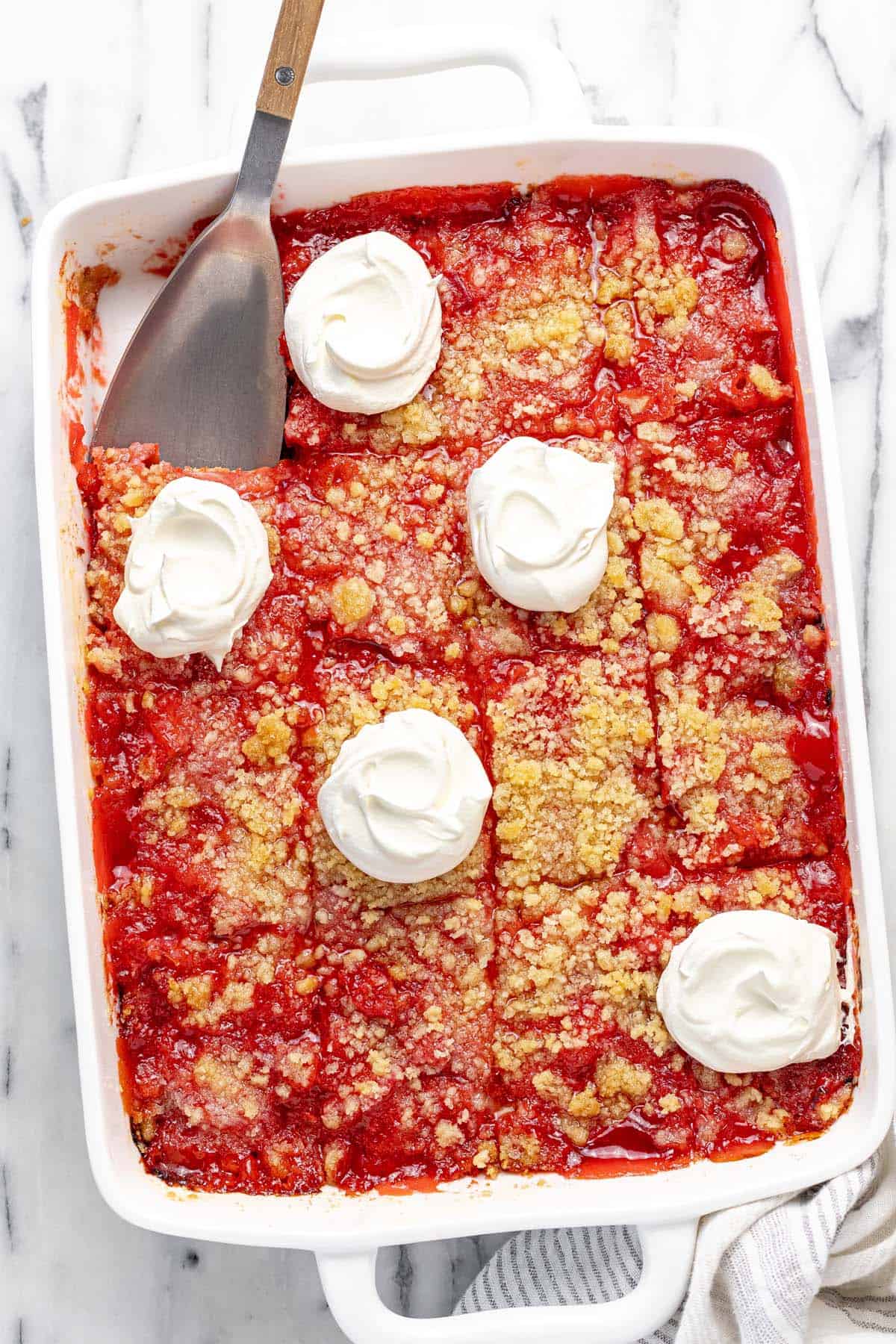 Large baking dish filled with rhubarb jello dessert, sliced and topped with cool whip. 
