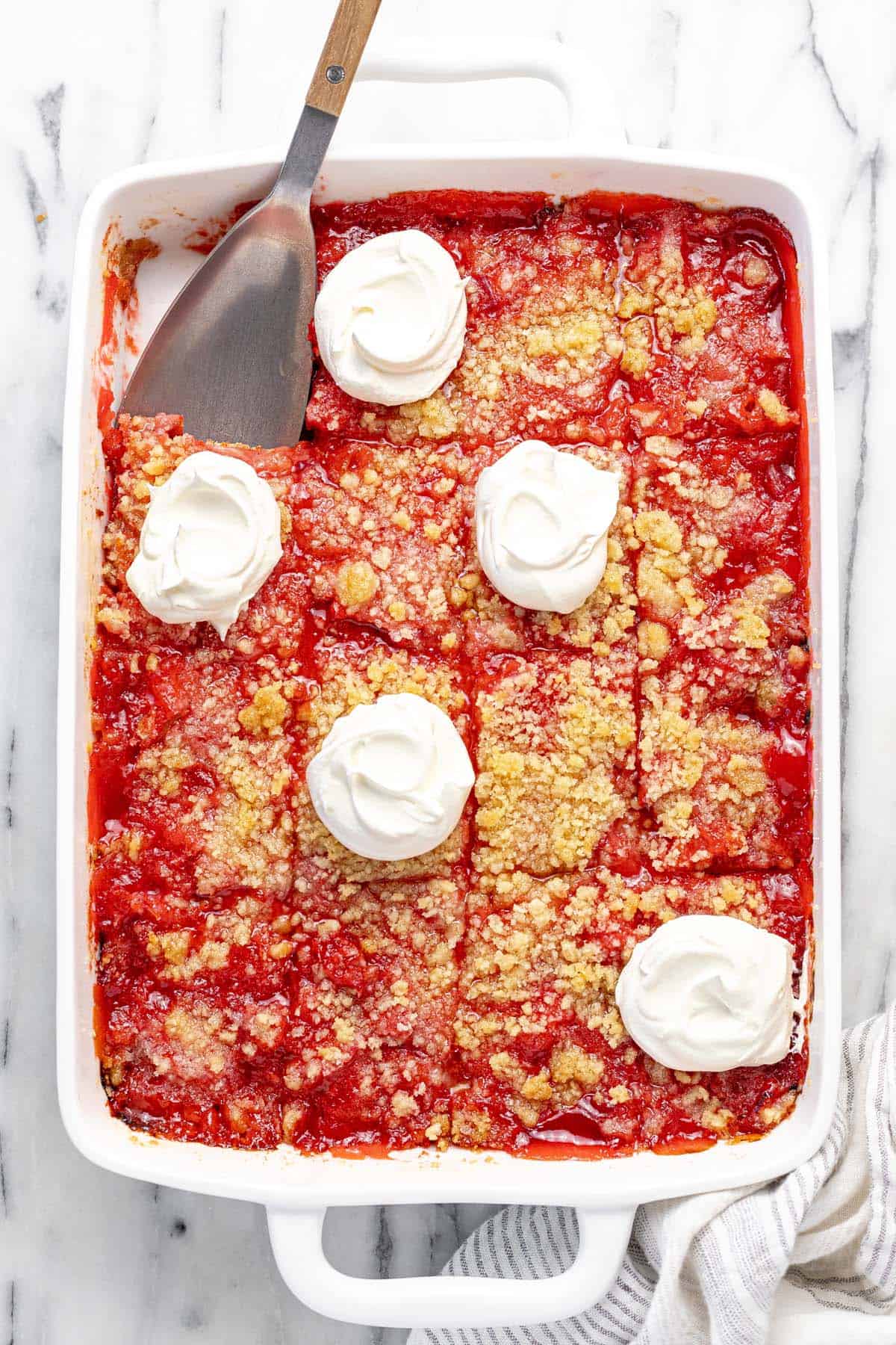 Large baking dish filled with rhubarb jello dessert, sliced and topped with cool whip.