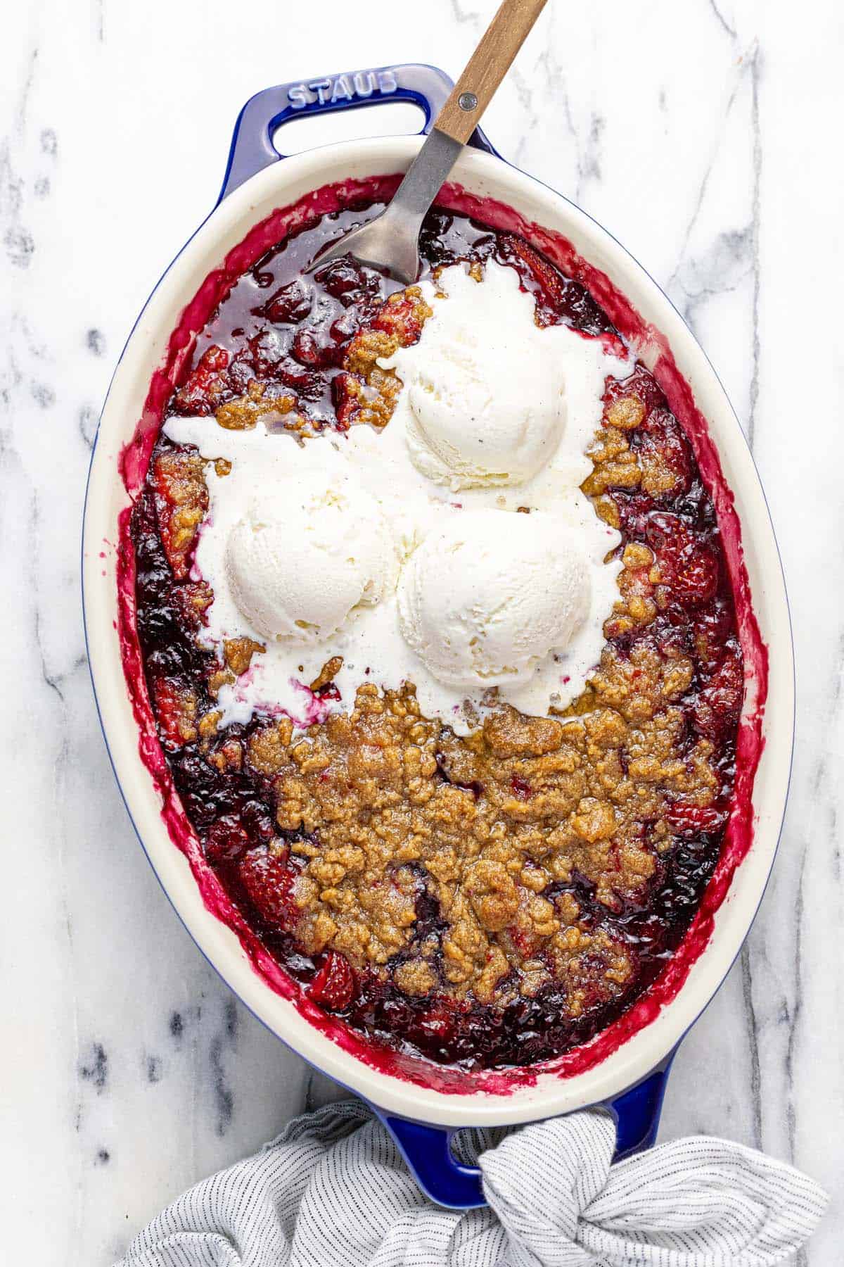 Baking dish filled with berry crumble topped with ice cream.