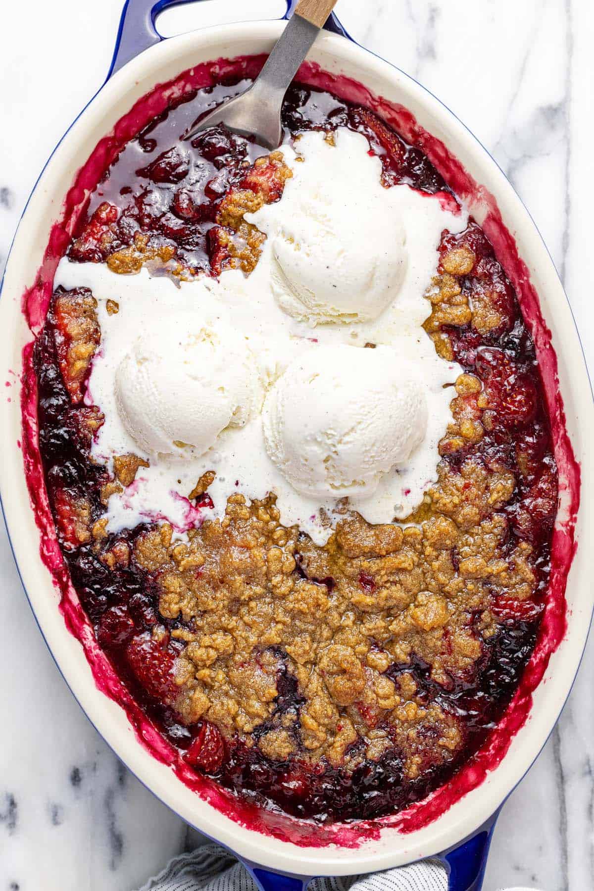 Baking dish filled with berry crumble topped with ice cream.