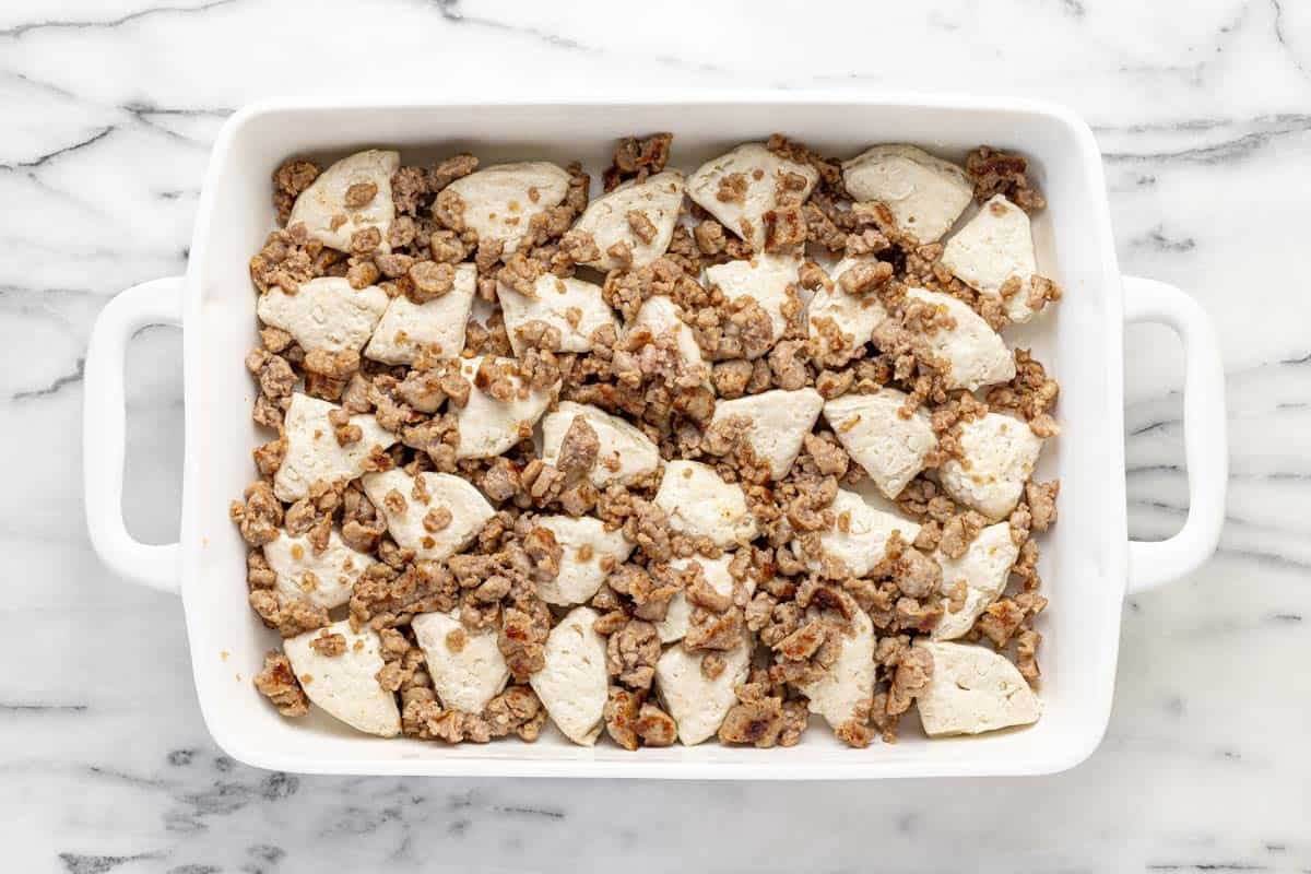 Baking dish filled with cut up biscuits and cooked sausage.