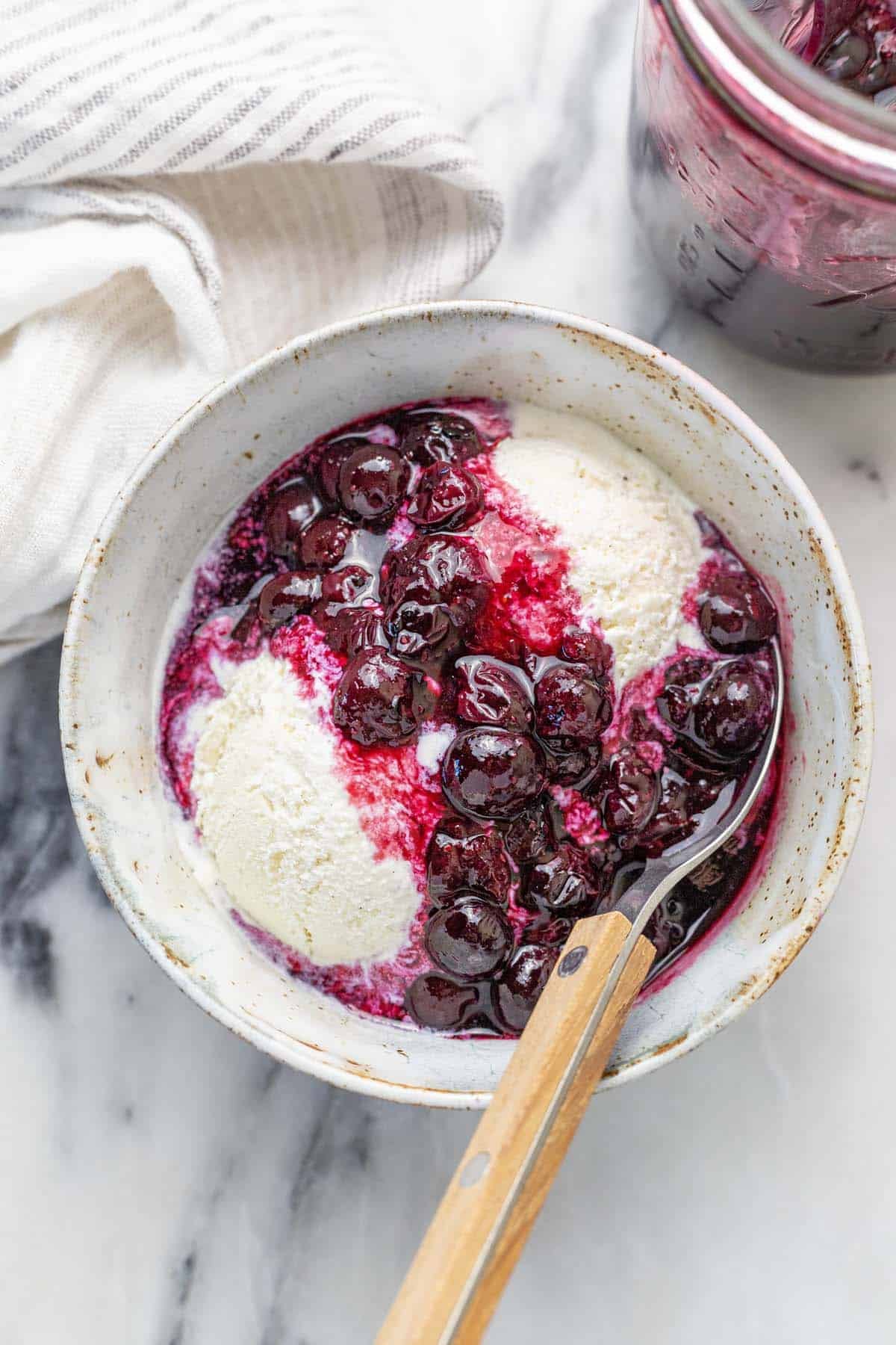 Bowl of ice cream topped with blueberry compote.