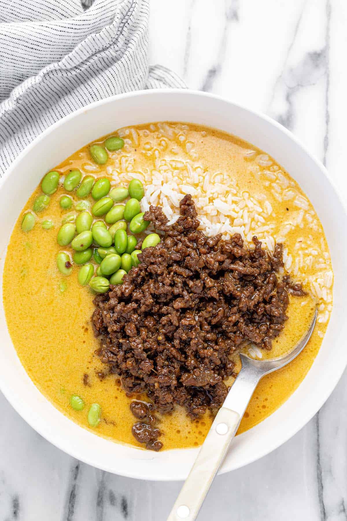 Bowl filled with brothy rice and ground beef with edamame.