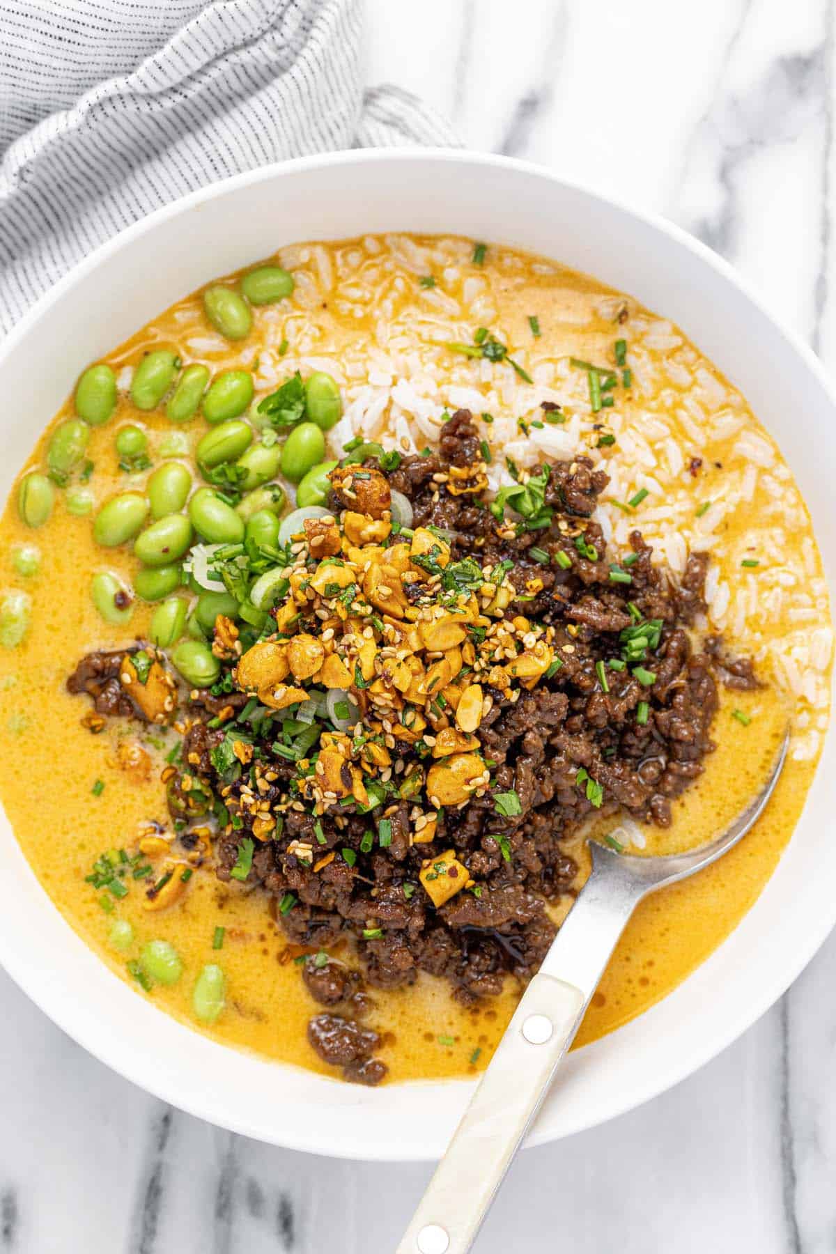 Bowl filled with brothy rice and ground beef topped with chopped peanuts.