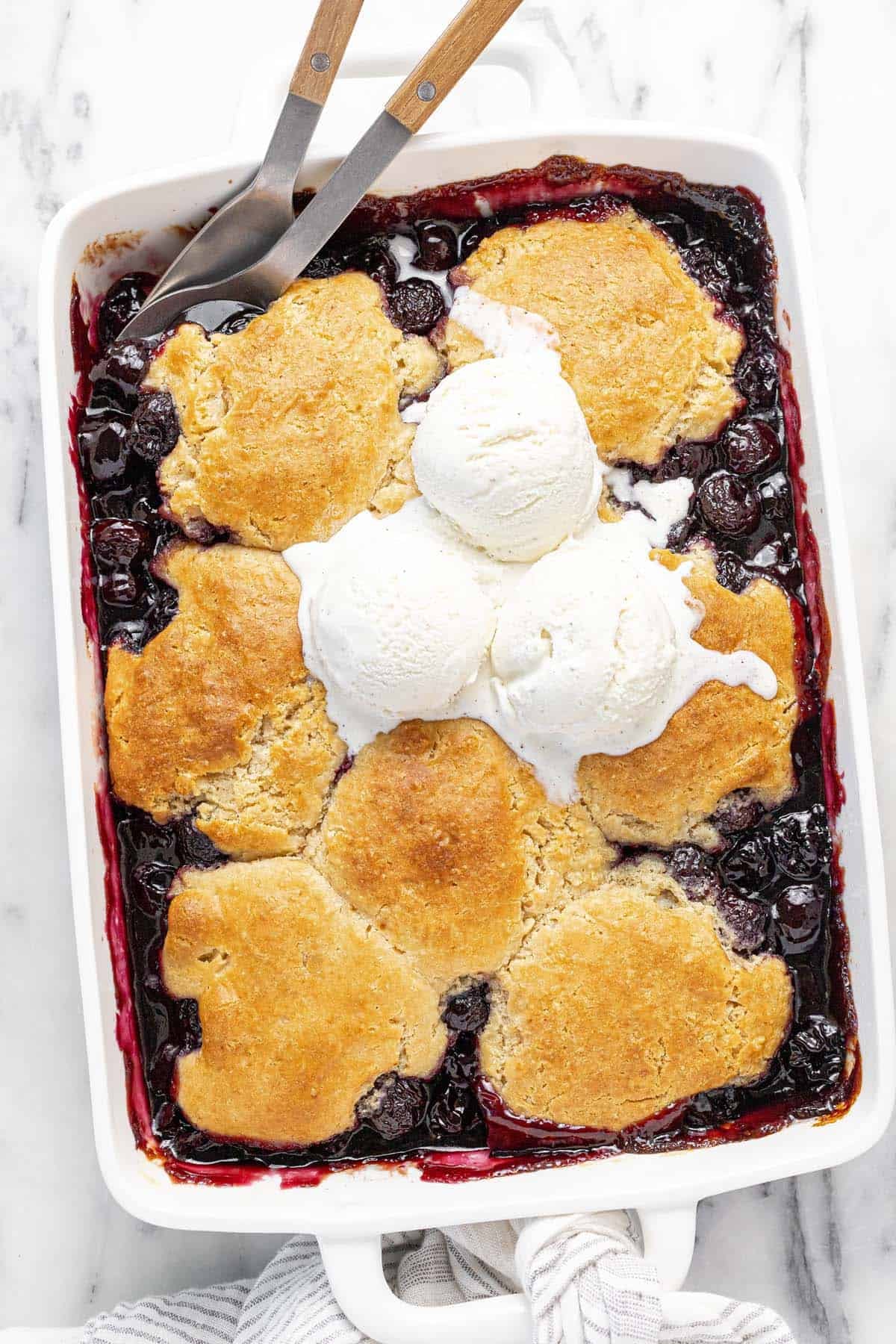 Large baking dish filled with cherry cobbler topped with three scoops of ice cream.