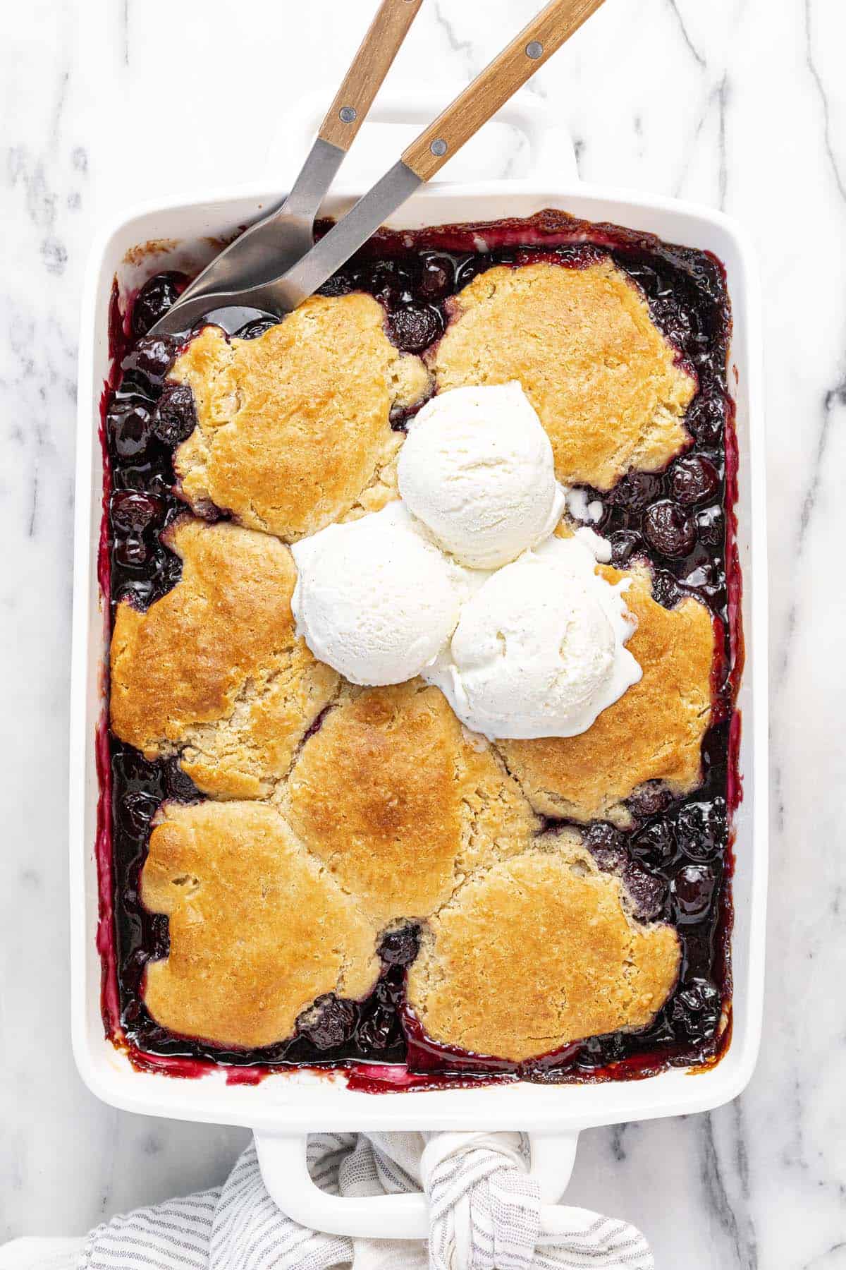 Large baking dish filled with cherry cobbler topped with three scoops of ice cream.