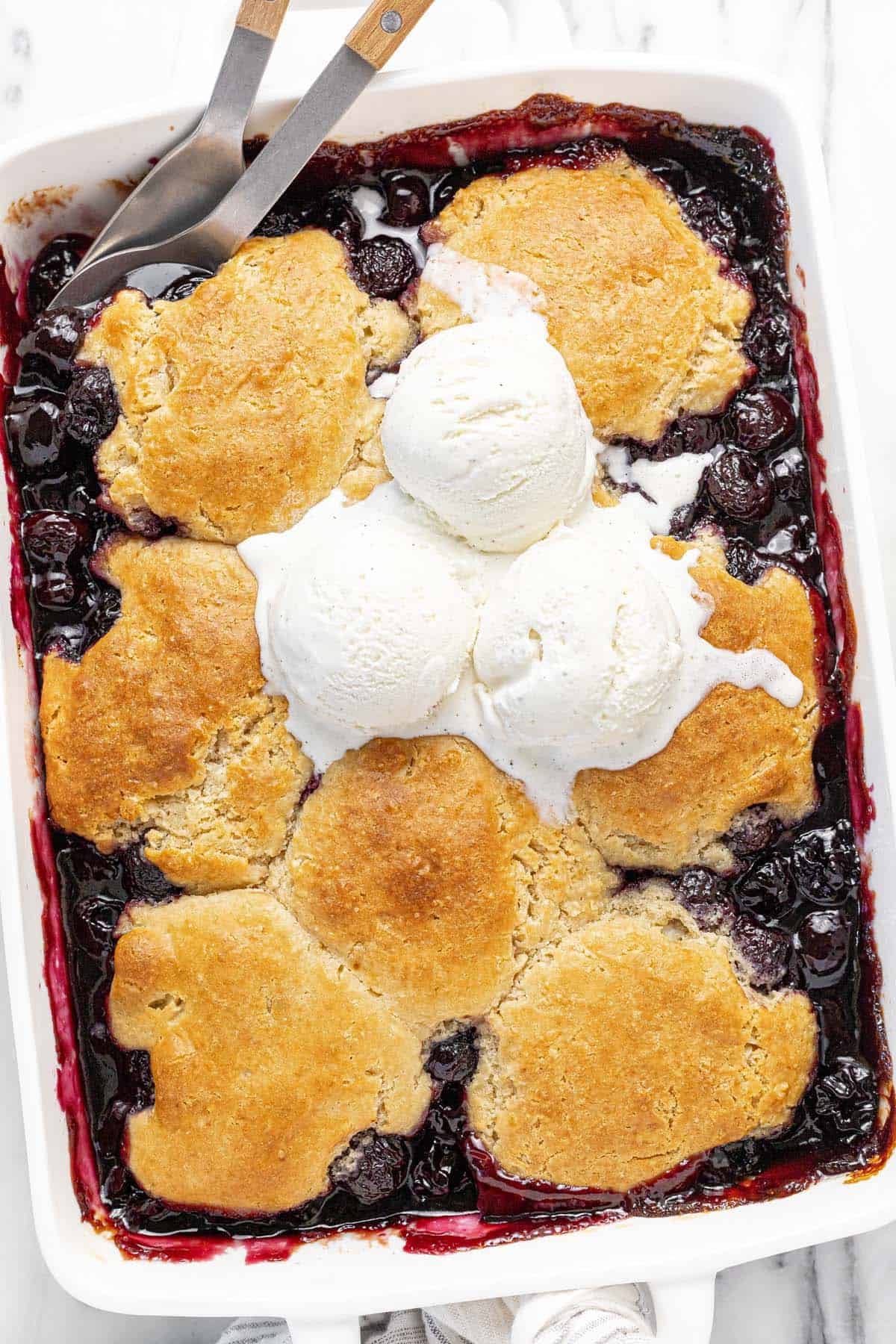 Large baking dish filled with cherry cobbler topped with three scoops of ice cream.