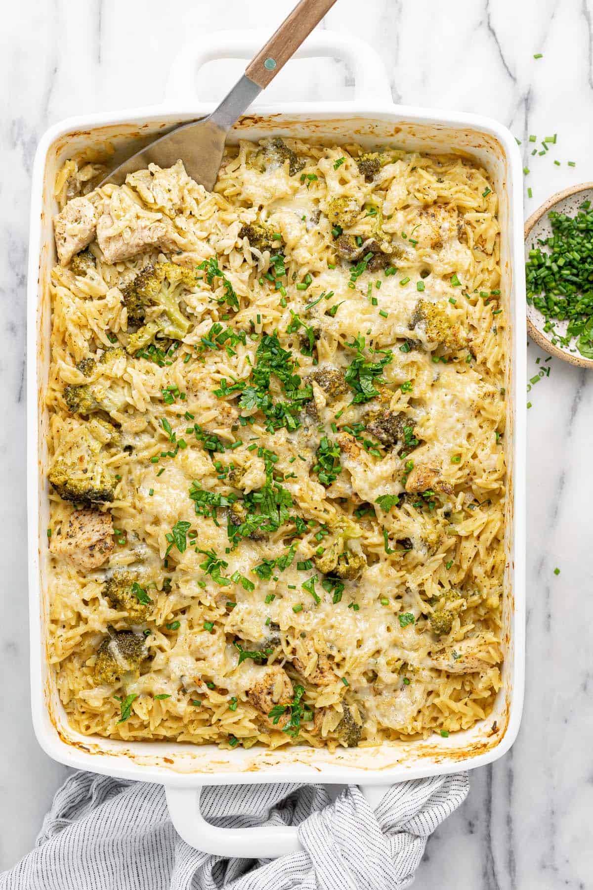 Large baking dish filled with baked chicken and orzo casserole garnished with fresh herbs.
