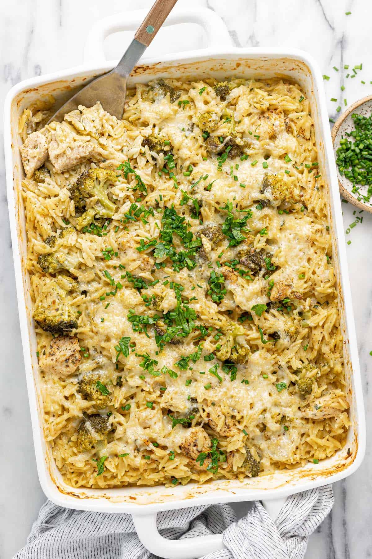 Large baking dish filled with baked chicken and orzo garnished with fresh herbs.
