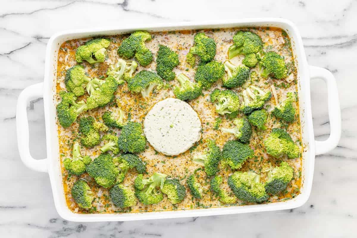 Broccoli and Boursin cheese added to a large baking dish with orzo pasta and sauce.