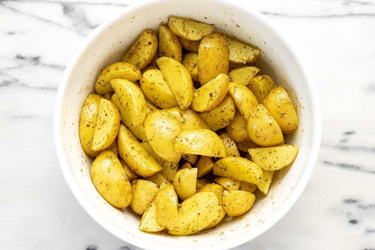 Large bowl of potatoes wedges tossed in oil and seasoning.