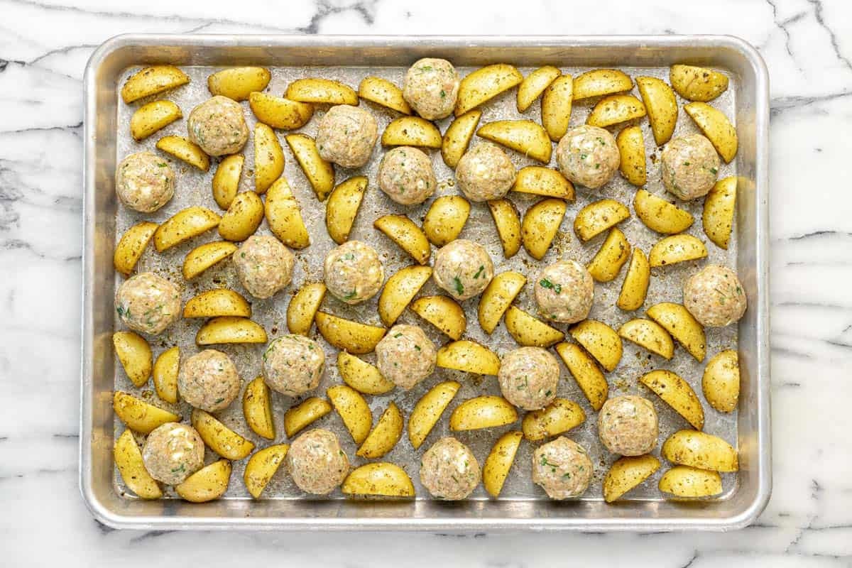 Partially roasted potatoes with meatballs on a sheet pan.