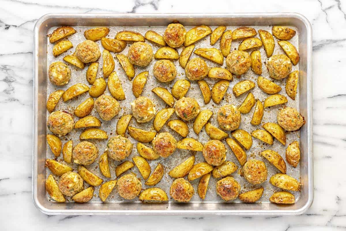 Freshly baked Greek chicken meatballs with roasted potatoes on a sheet pan.