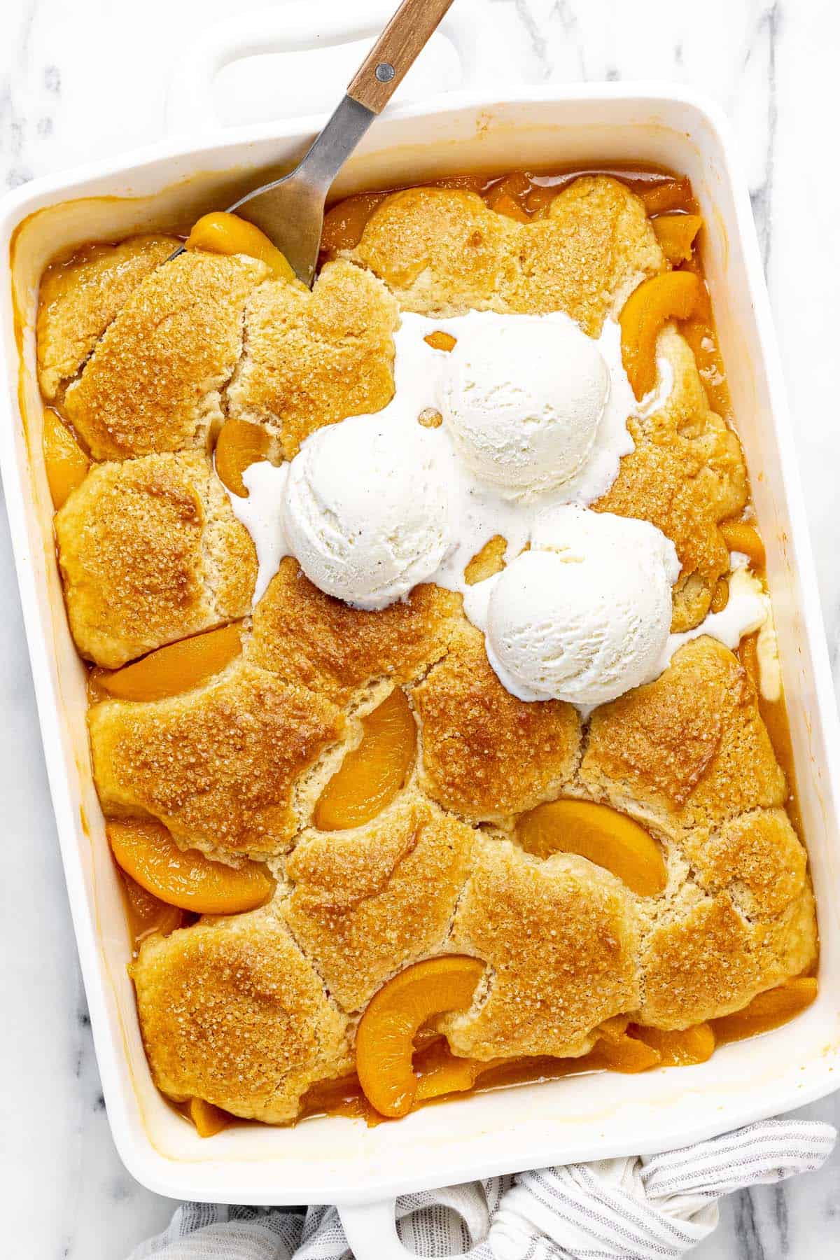 Large baking dish filled homemade peach cobbler topped with vanilla ice cream.