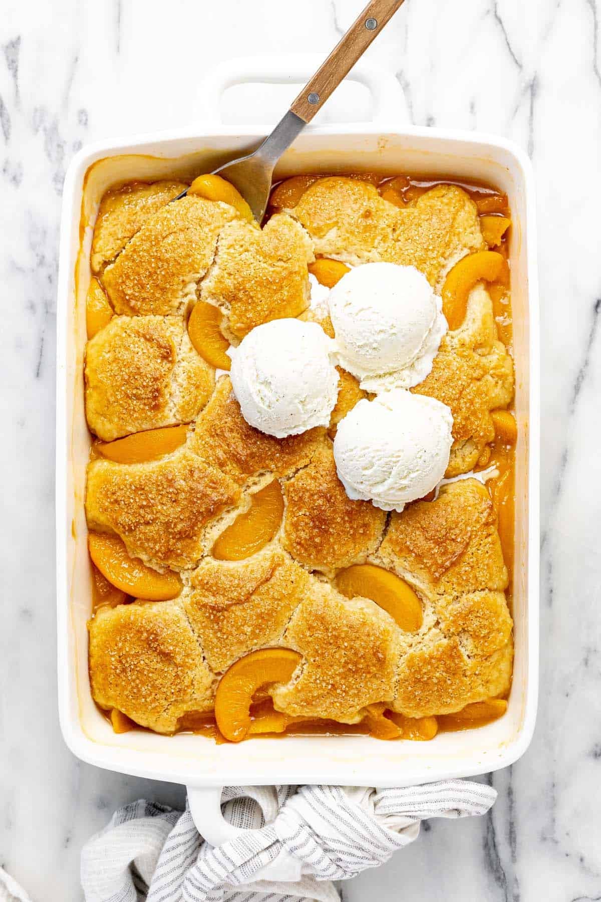 Large baking dish filled homemade peach cobbler topped with vanilla ice cream.