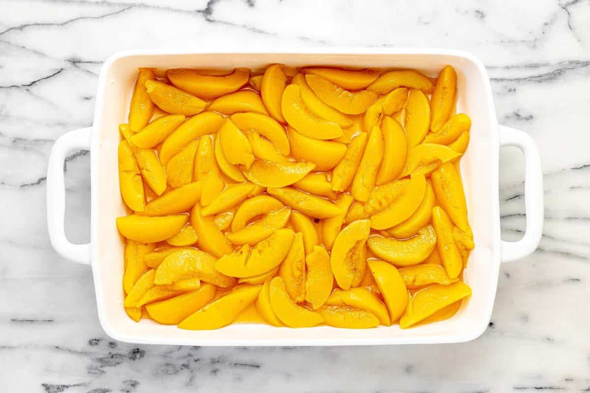 Baking dish filled with sliced peaches, sugars, and vanilla.