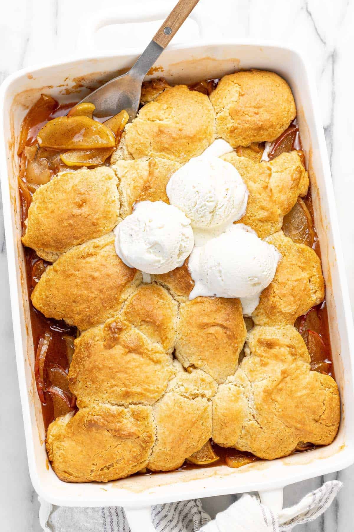 Large pan filled with homemade apple cobbler topped with vanilla ice cream. 