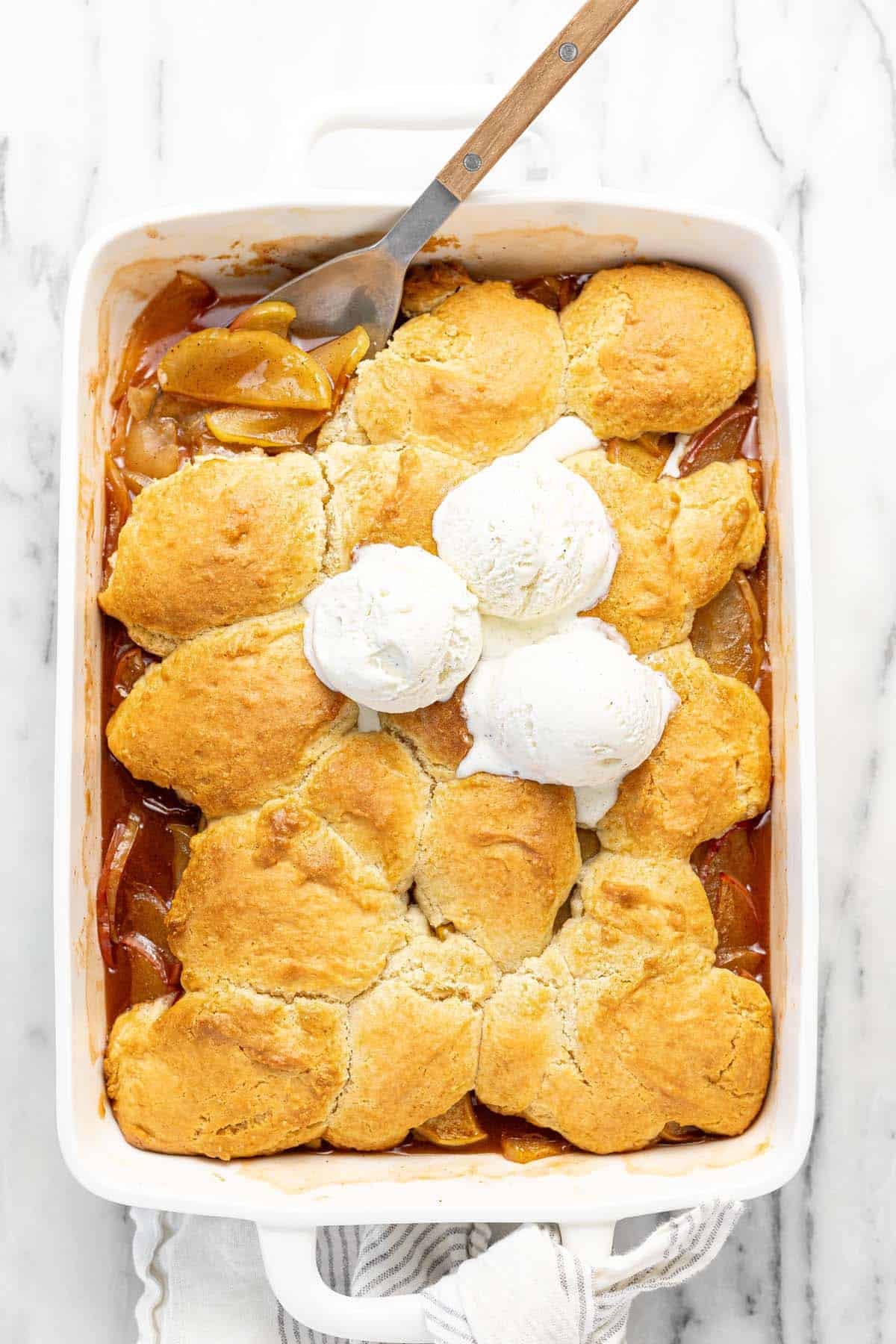 Large pan filled with homemade apple cobbler topped with vanilla ice cream. 