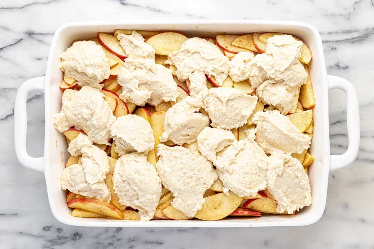 Dollops of cobbler batter on top of sliced apples in a baking dish. 