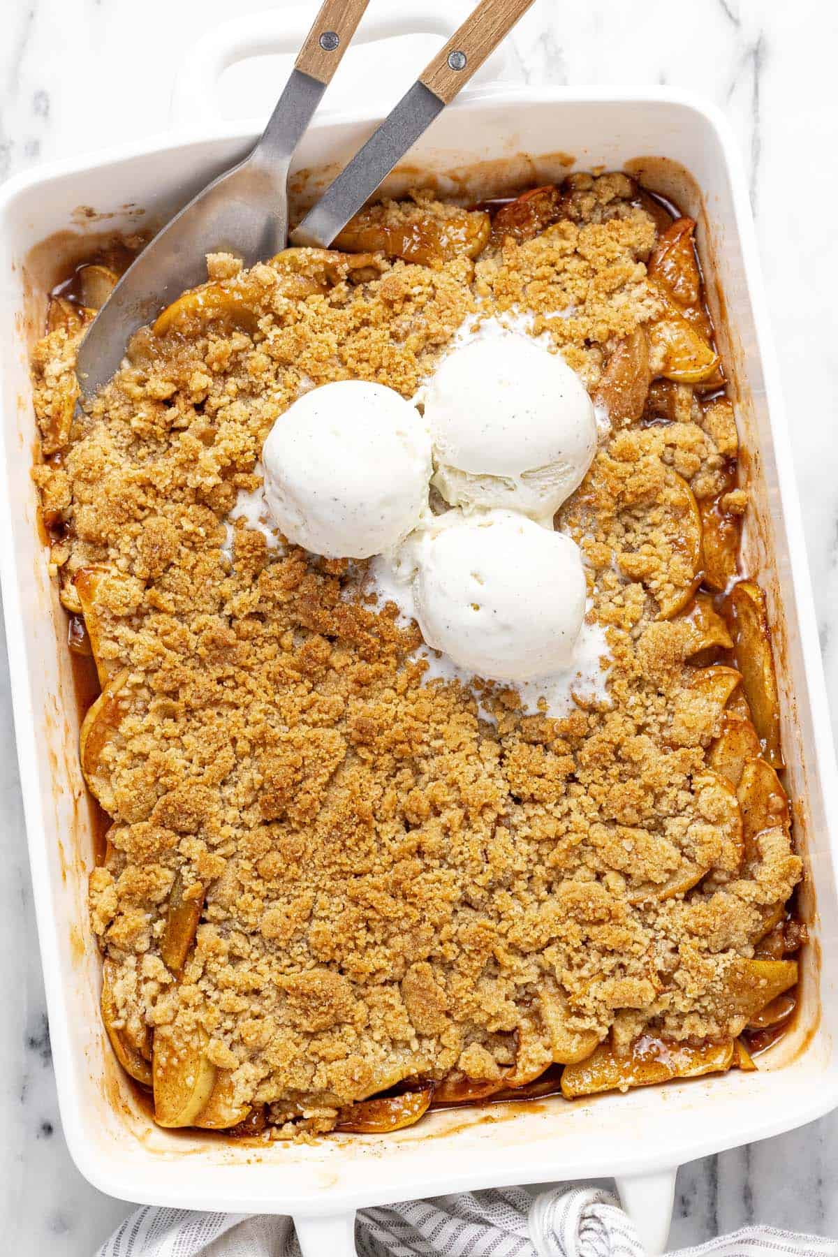 Large pan filled with homemade apple crumble topped with scoops of vanilla ice cream.