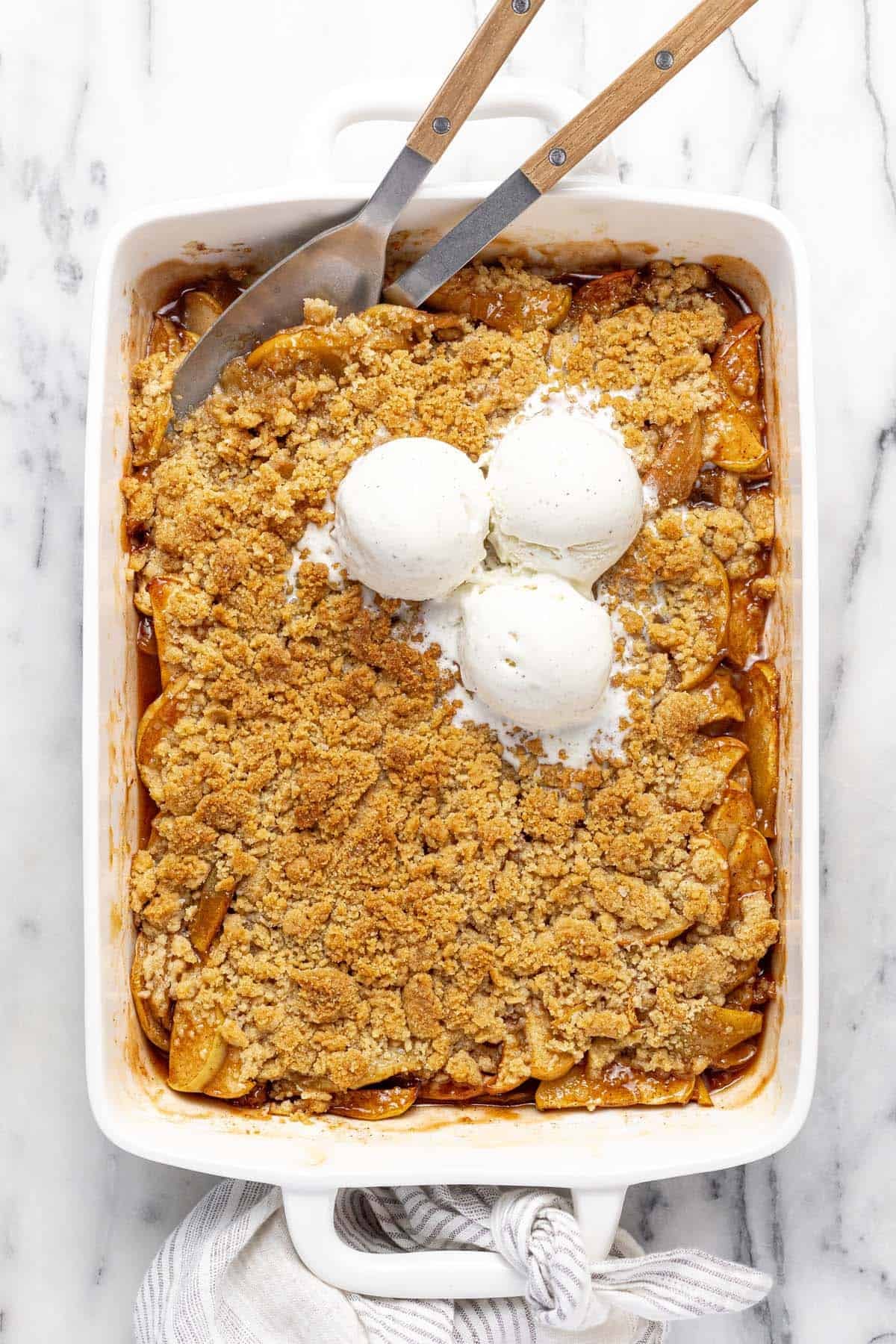 Large pan filled with homemade apple crumble topped with scoops of vanilla ice cream.
