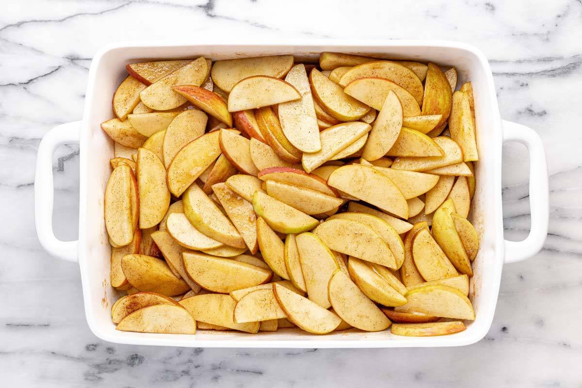 Large baking dish filled with sliced apples tossed in sugar and spices.