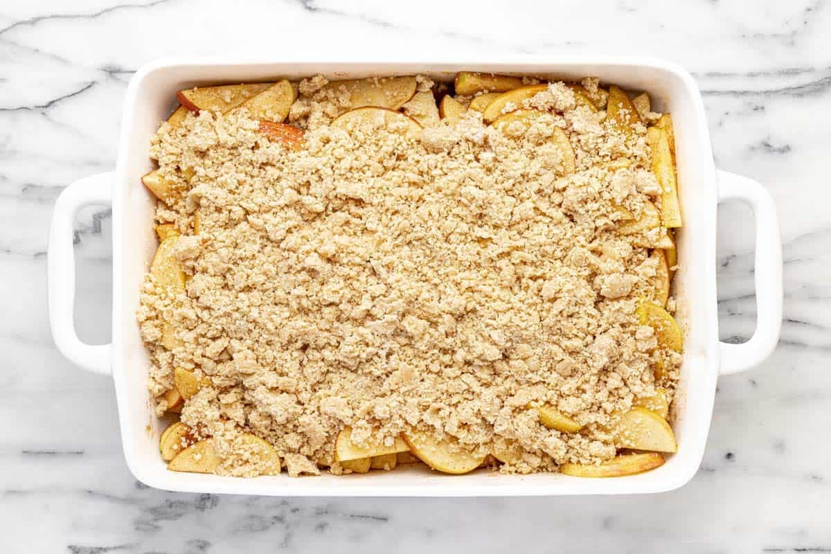 Crumble topping on top of sliced apples in a large baking dish.