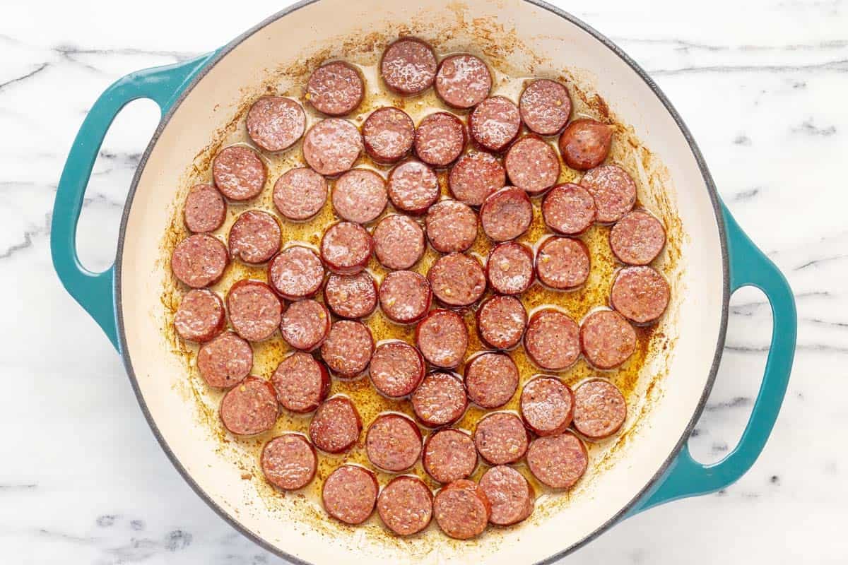 Seared sausage rounds in a large pan.