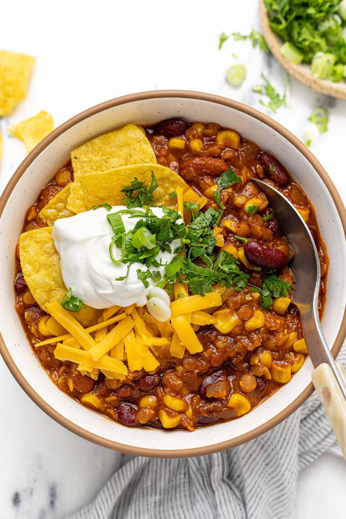 Bowl of vegetarian chili topped with sour cream, tortilla chips, cheese, and cilantro.