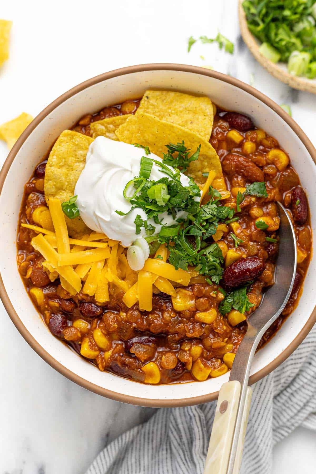 Bowl of vegetarian chili topped with sour cream, tortilla chips, cheese, and cilantro.